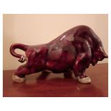 Red glazed ceramic charging bull or ox sculpture, vibrant, glossy oxblood or crimson red glaze with lighter mottled accents and a dynamic, low-slung charging posture.