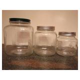 2 Hoosier-style glass canisters, classic square-sided shape with rounded shoulders and distinctive vertically ribbed corners. 8" & 6.75" T, 6" & 5" W. 8/15/26 added 1 more jar, smaller just found, mak