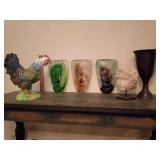 3 art glass face masks, green, brown, purple. A ceramic purple rooster, limestone angle boy or putto head and a bronze chalice/vase.