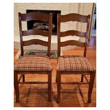 Two wooden ladder-back dining side chair features a medium brown warm stain and a padded seat upholstered in a rustic red, yellow, and green plaid fabric. 18.5 x 16.75 x 40 in tall. Seat height is 19 