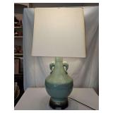 Chinese Longquan-style celadon porcelain table lamp features a soft seafoam green glaze, molded floral and lotus petal relief carvings, and distinctive elephant or dragon-mask ring handles mounted on 