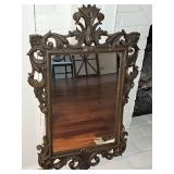Vintage Rococo-style decorative wall mirror features an ornate dark brown scroll and acanthus leaf crest frame. 21x33.5 in tall.