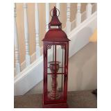 Tall red decorative metal lantern featuring an internal pillar candle holder - left side is missing glass panel - 20” tall