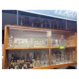 Cabinet full of drinking glasses, bottles w liquid, Olympia beer poster
