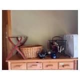 Wrought iron magazine rack with reading material, laundry basket, suitcase rack, box fan, and a few home decor items