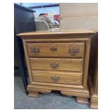 Traditional three-drawer golden oak nightstand.