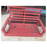 A weathered red wooden slat porch swing with