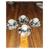 Vintage black ceramic espresso or demitasse cups and saucers featuring a colorful floral design and gold rims