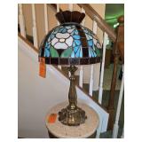 Tiffany-style stained glass table lamp featuring a floral domed shade and an ornate, lily-pad style sculpted bronze base.
