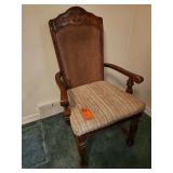Country French-style cane back dining arm chair featuring an ornate carved wooden crest and a textured, neutral-striped upholstered seat