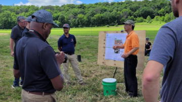 Wei Zheng (orange shirt) and Rabin Bhattarai (left of poster) speak about biochar at a field day.