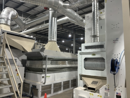 Seed moves from a bucket elevator to three hoppers to be blended in batches as inoculants, microbes, and other beneficial additives are applied to the seed, which is then dried.