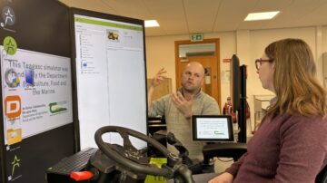 Professor Florence Becot, US farm safety expert is pictured seated on one of the Department of Agriculture, Food and the Marine (DAFM)–funded machinery simulators in Teagasc Ashtown, Dublin, ahead of a Teagasc seminar addressing the “Farm Risk Paradox”. Also pictured is Paddy Smith, College Lecturer, Teagasc, College of Amenity Horticulture, National Botanic Gardens, who is providing an overview of the simulator. Image courtesy of Teagasc.