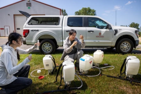 Undergraduate student Ruiying Wang, left, and graduate student Mingda Wu measure out precise amounts of beneficial bacteria for mixing into backpack sprayers at Hancock Agricultural Research Station in Hancock, Wis. Image courtesy of University of Wisconsin-Madison.