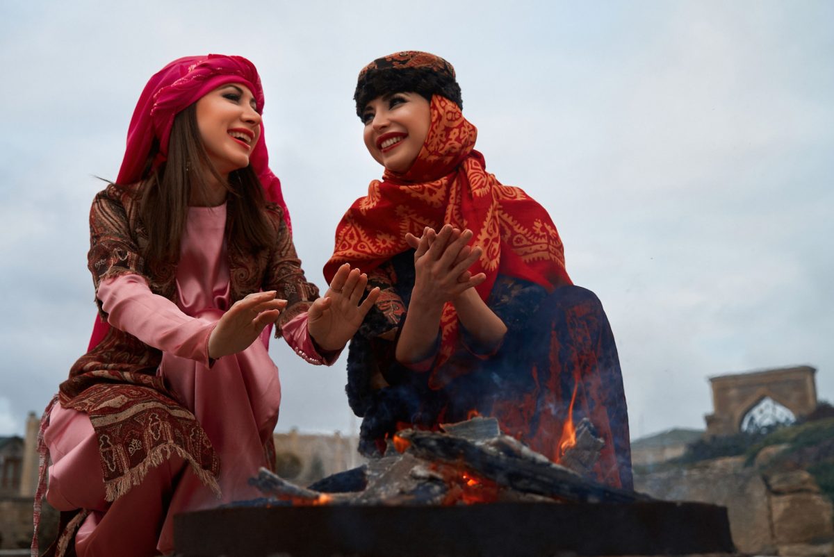 Iran Beautiful azeri women in traditional Azerbaijani dress warming hands above the bonfire