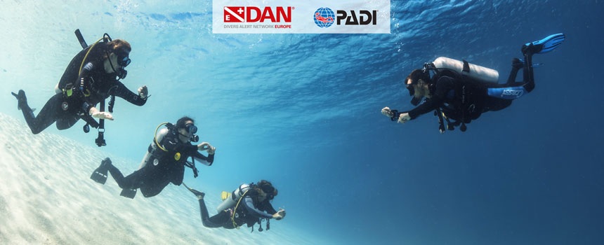 Group of scuba divers swimming underwater with DAN and PADI logos