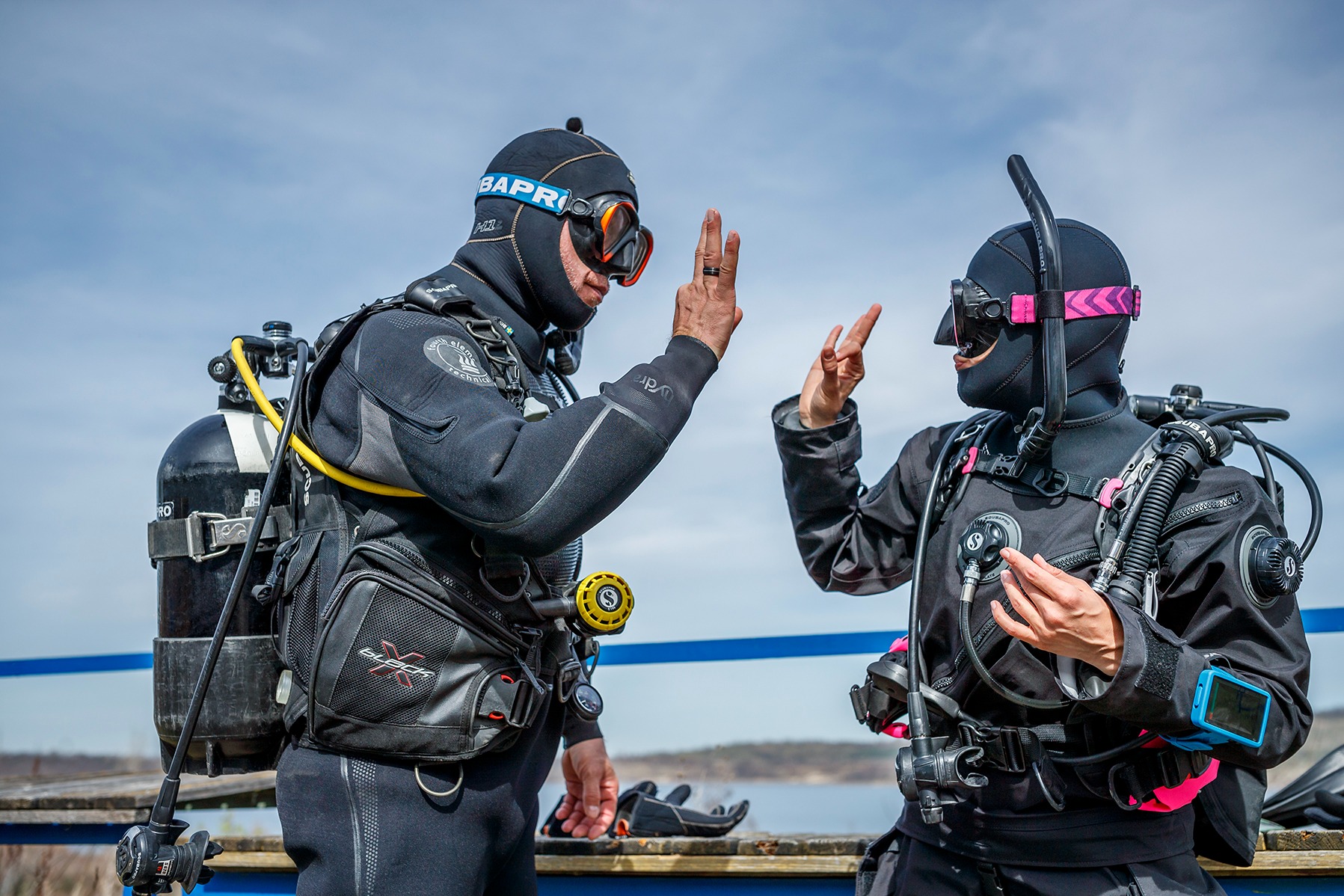 Two equipped divers reviewing hand signals on a dock