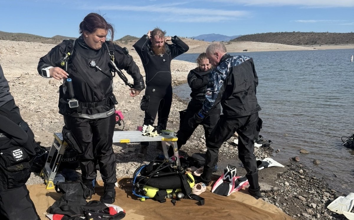 New divers donning drysuits with scuba gear laid out on the shore of an Arizona lake