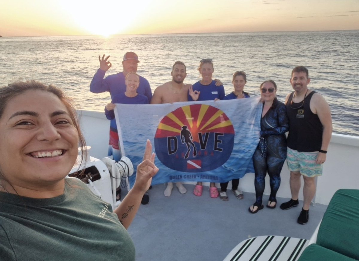 Dive Arizona group holding the shop flag on a boat at sunset during a warm-water dive trip