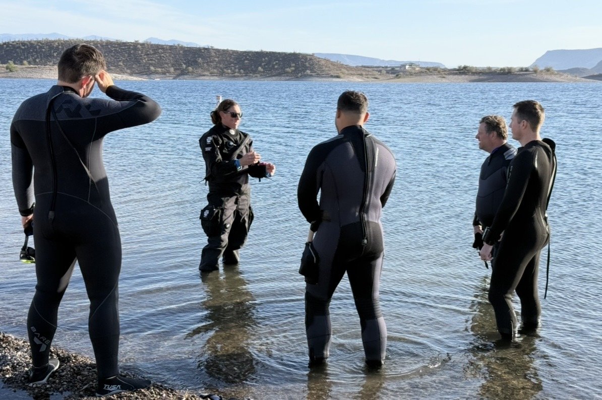 Dive Arizona instructor briefing wetsuit-clad students at the water's edge before a training dive