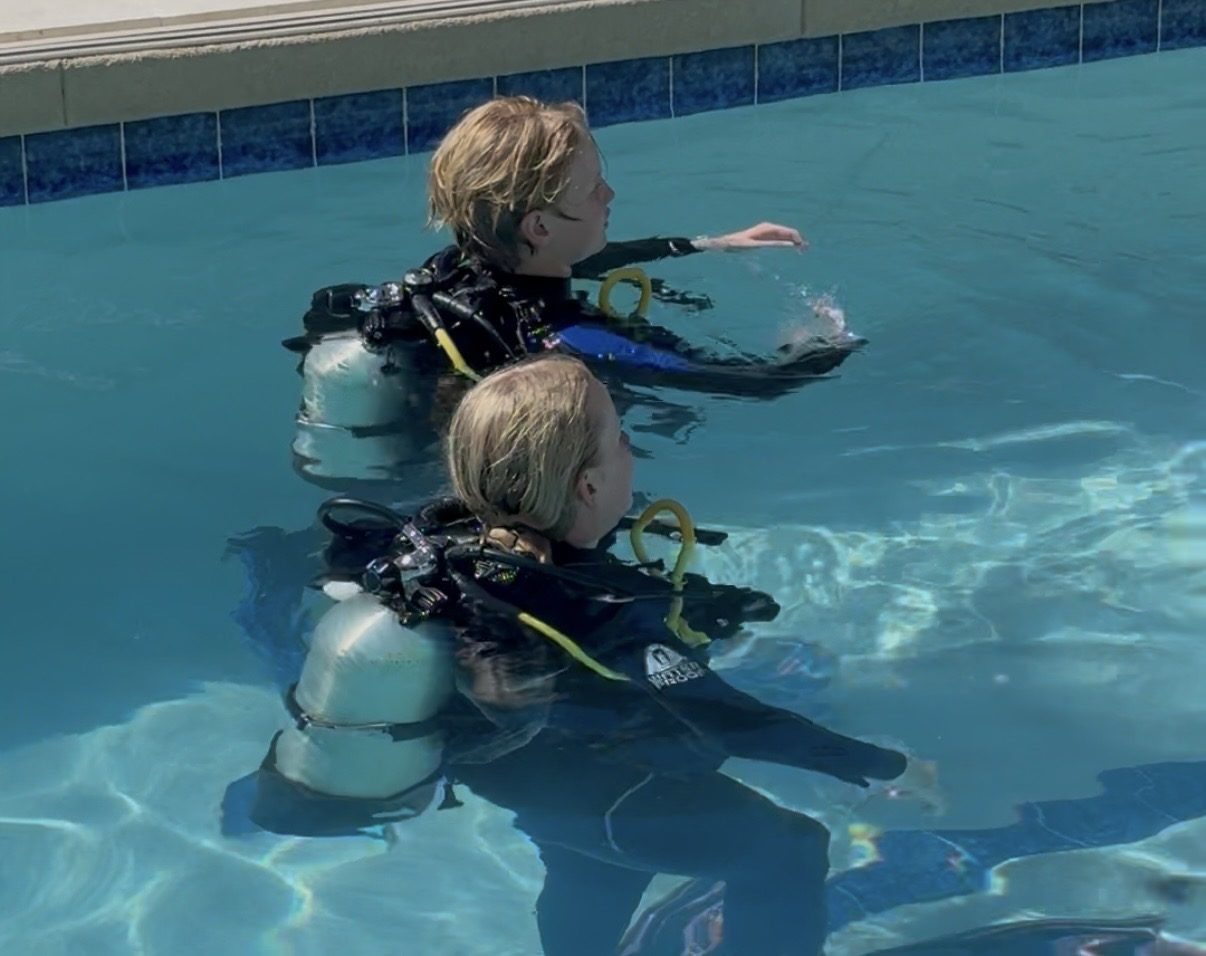 Two junior divers in full scuba gear practicing in the pool