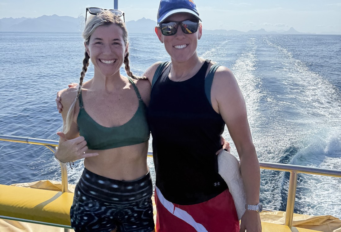 Two divers standing on a boat deck with the ocean wake behind them on a group dive trip