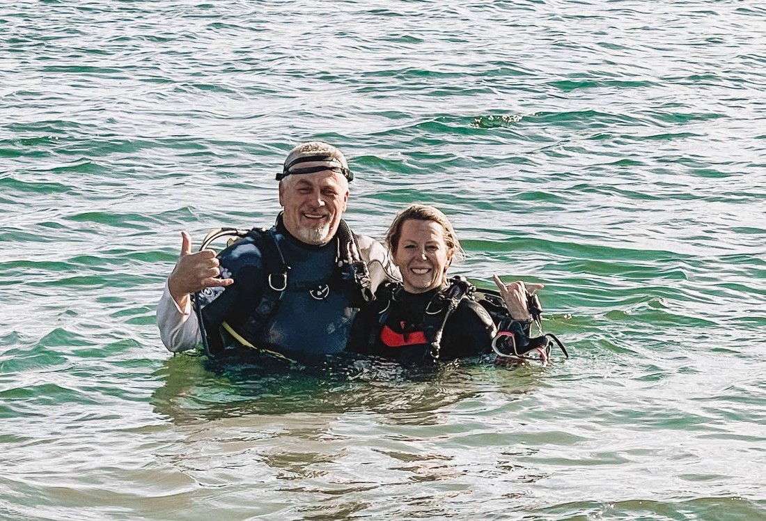 Two divers in wetsuits smiling together in the water on a lake dive