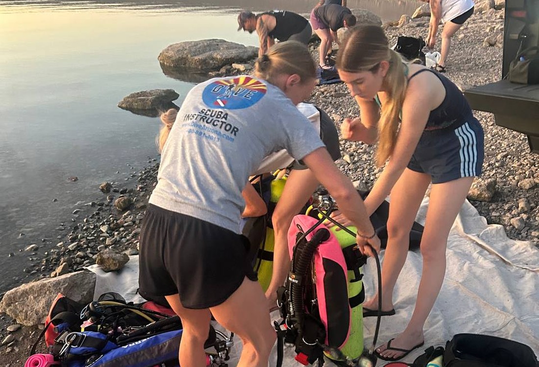 A Dive Arizona scuba instructor helping a student set up gear one-on-one on the shore of a lake