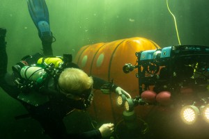 Scientific Diver interacts with robotic vehicle outside of Ocean Space Habitat (background).