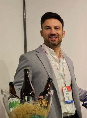 Pedro Oliveira smiling in a gray blazer with beer bottles