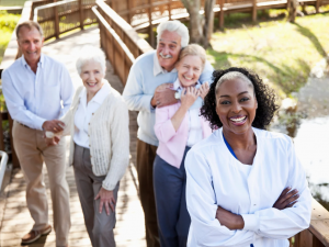 A woman caregiver smiling with the happy senior residents in the back