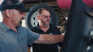navy blue polo shirts by tire car lift looking at black screen