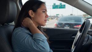 Woman experiencing neck pain while driving after a minor car accident on a Texas highway.