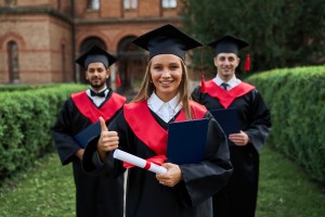 graduate female shows like with her friends graduation gowns holding diploma smiling camera