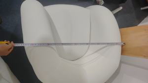 A tape measure is used to check the width of an upholstered lounge chair. ALT: A tape measure stretc