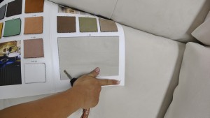 An upholstery swatch is compared with a sofa surface to check color and texture consistency.