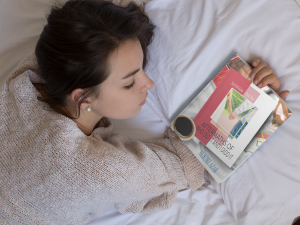 young-girl-holding-a-book-on-her-hand-while-lying-down-on-her-bed-mockup-a14275