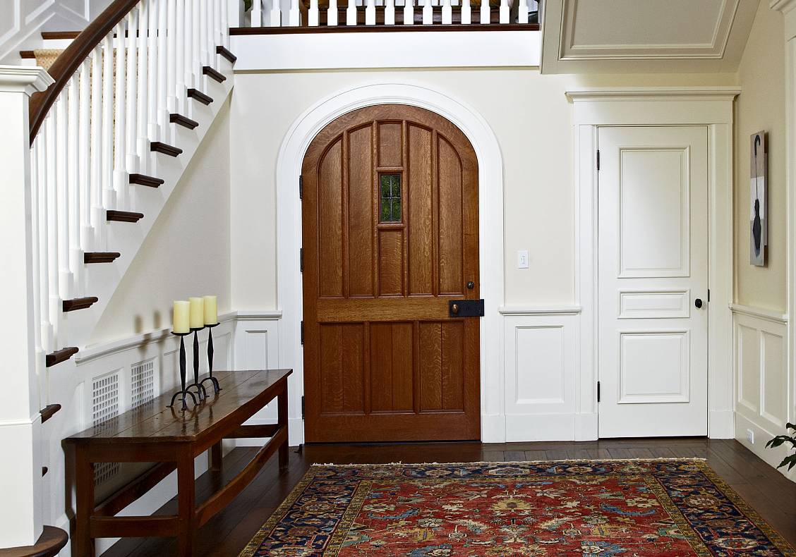 English country entry hall with curved stair, walnut floors, quartersawn white oak arched entry door with leaded glass panel, and family dog Cassie.