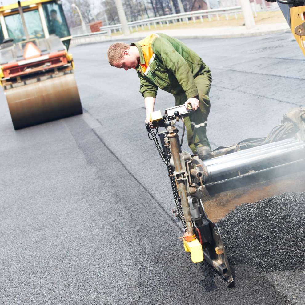 Careers Page Asphalt Paving Background Image An asphalt paver lays hot asphalt along a stretch of road.