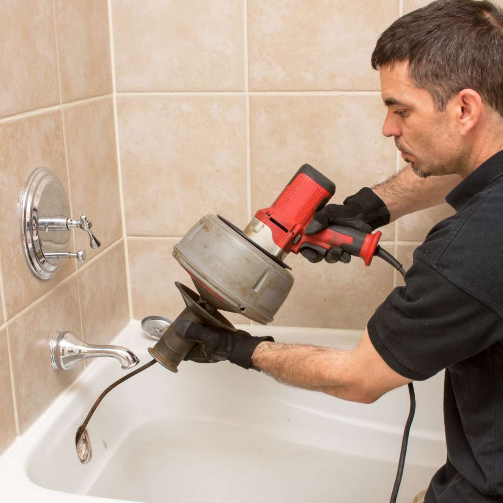 Careers Page Advanced Plumbing Background Image A plumber uses a drain cleaning tool on a shower drain.