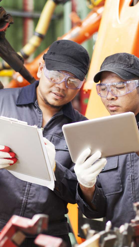 Careers Page Manufacturing Technology Background Image A pair of manufacturing technicians compare notes on a clipboard and a tablet.