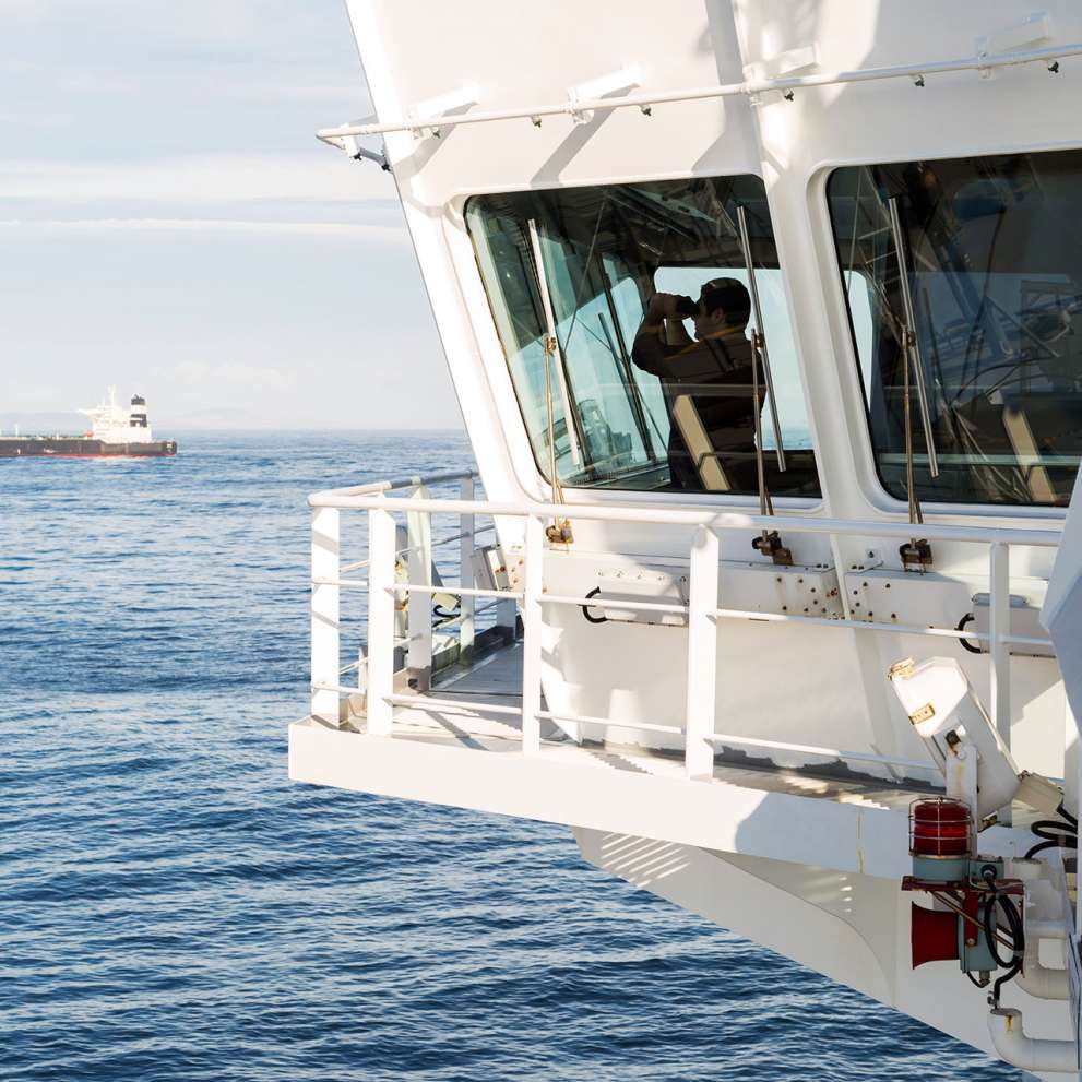 Careers Page Seamanship Background Image A seaman looking through binoculars at helm of large cargo ship