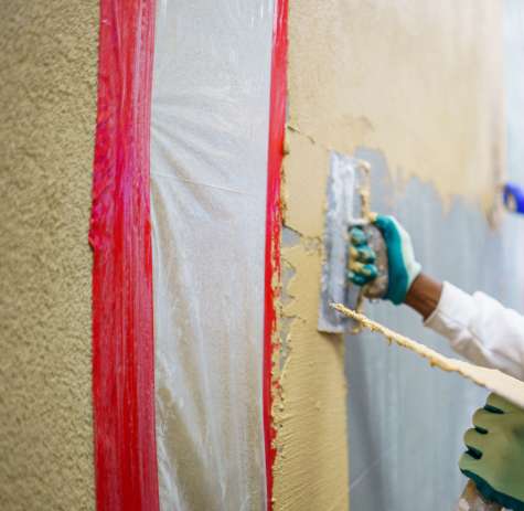 A plastering technician applies a coat to a wall.