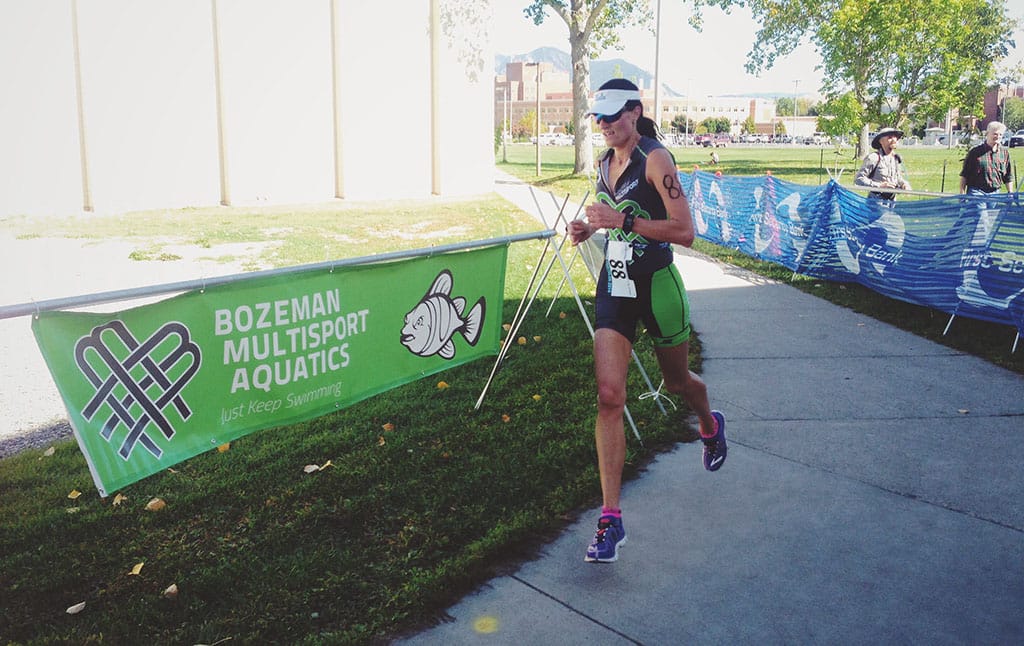 Milica McDowell running in front of a Bozeman Multisport Aquatics banner at the Montana State University Triathlon wearing a Montana Multisport tri kit