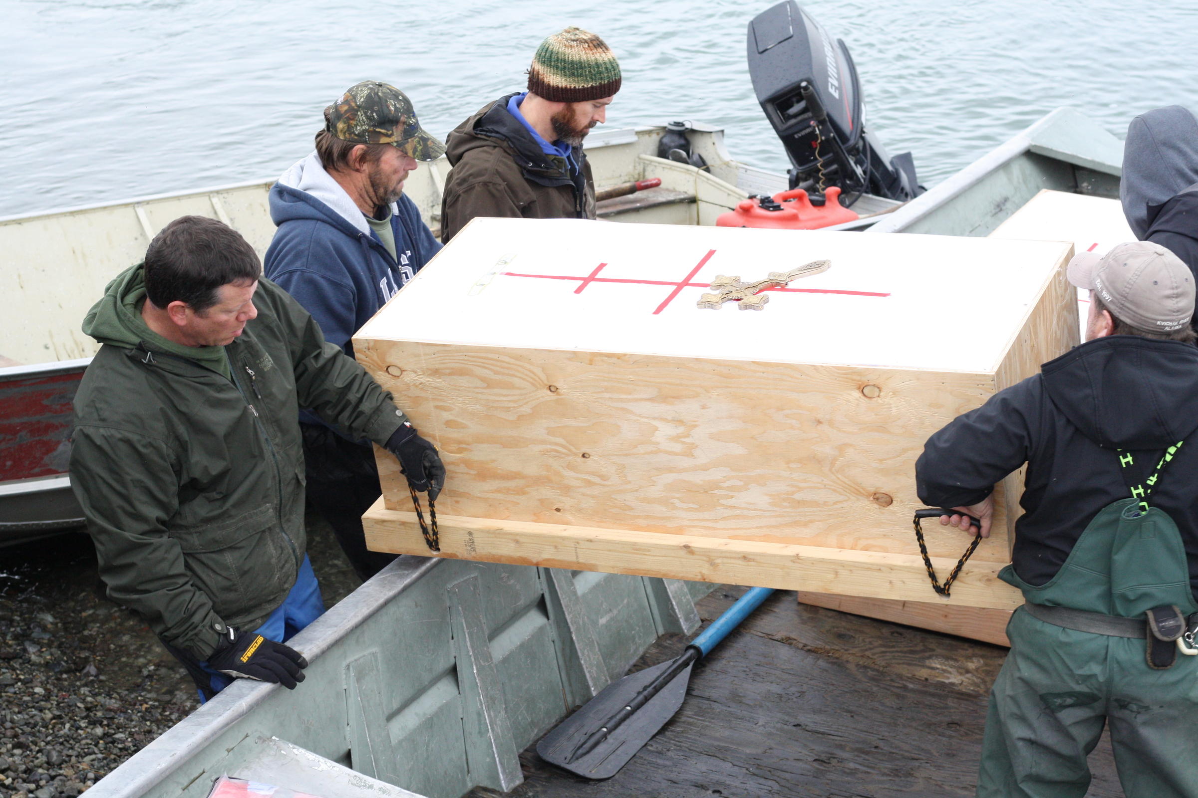 Several people place the coffins in a skiff for the final piece of their journey from Igiuigig to the old village site of Qinuyang. (Photo by Avery Lill/KDLG)