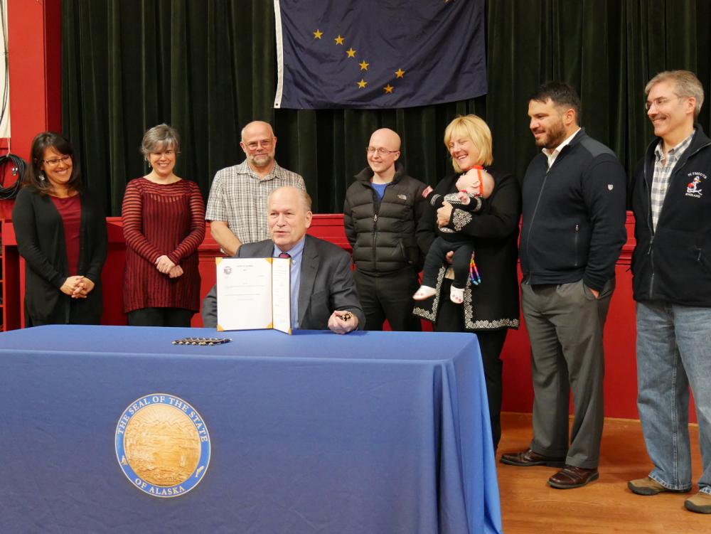 Alaska Gov. Bill Walker signs Senate Bill 28 on Thursday, November 16, 2017, at Petersburg’s Sons of Norway Hall. Behind him are legislative staffer Melissa Kookesh, Petersburg community and economic development director Liz Cabrera, mayor Mark Jensen, Rep. Jonathan Kreiss-Tomkins, Petersburg harbormaster Glo Wollen and daughter Sigrid, legislative aide David Scott and lobbyist Ray Matiashowski. (Photo by Joe Viechnicki/KFSK)