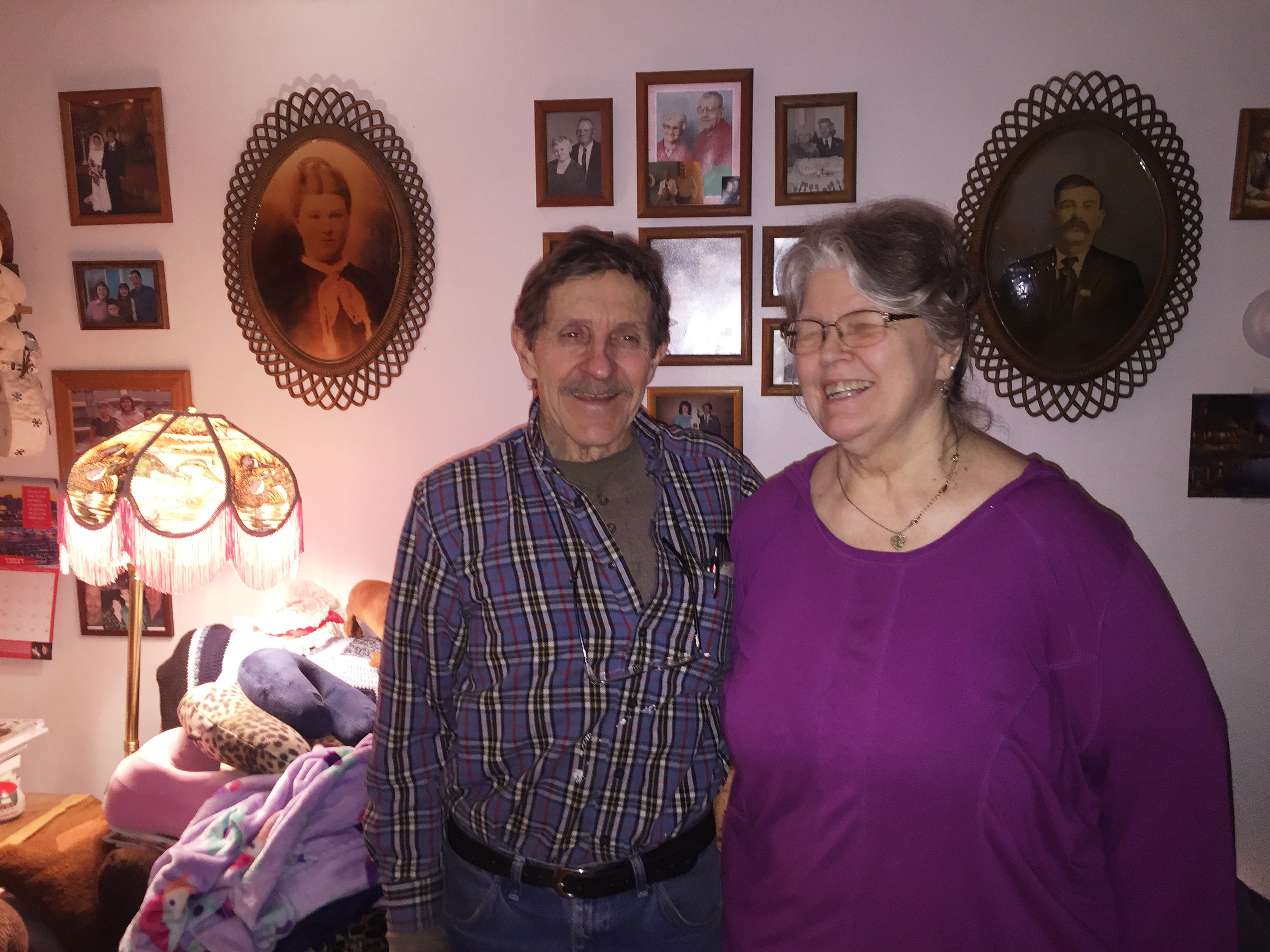 Shirley and Tom Clements tease each other as they pose in front of their wall of memories. (Photo by Anne Hillman/Alaska Public Media)