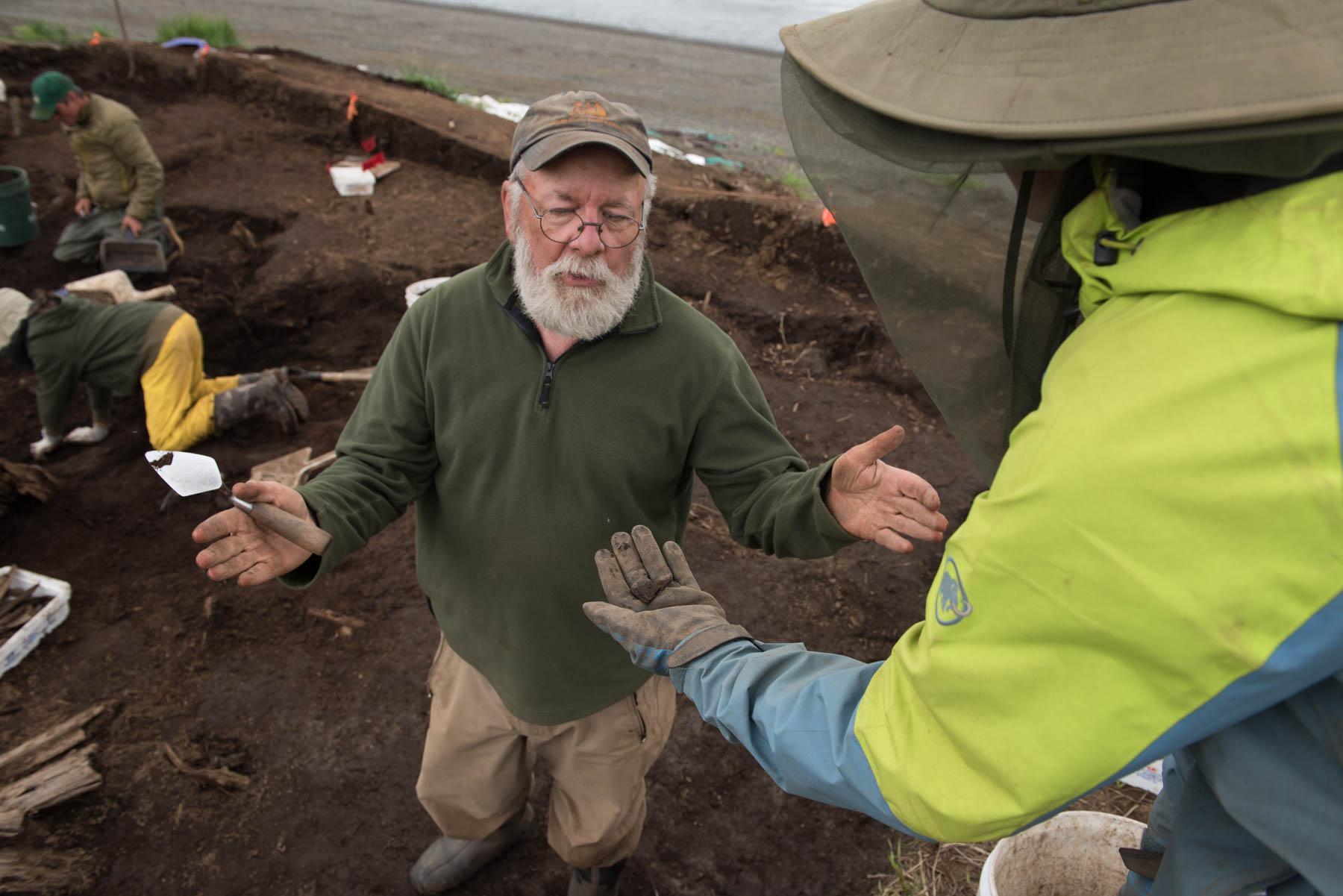 Dr. Rick Knecht explains July 24, 2018, the purpose of a small triangular piece of leather to student Lauren Phillips while digging at the Nunalleq site . The leather is likely caribou hide and was used to patch a larger piece of hide or clothing. (Photo by Katie Basile/KYUK)