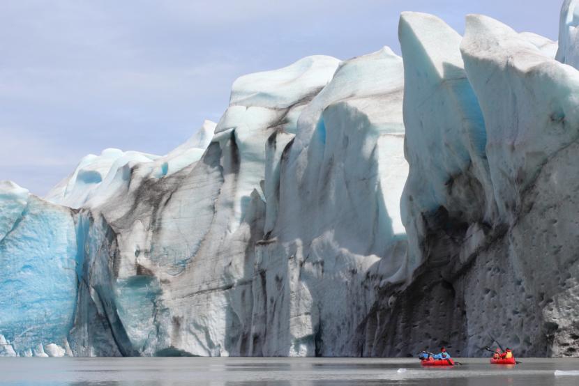 Two small boats row past the Grewingk Glacier.