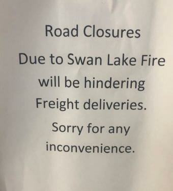 A sign that says, "Road Closures Due to Swan Lake Fire will be hindering freight deliveries. Sorry for any inconvenience."